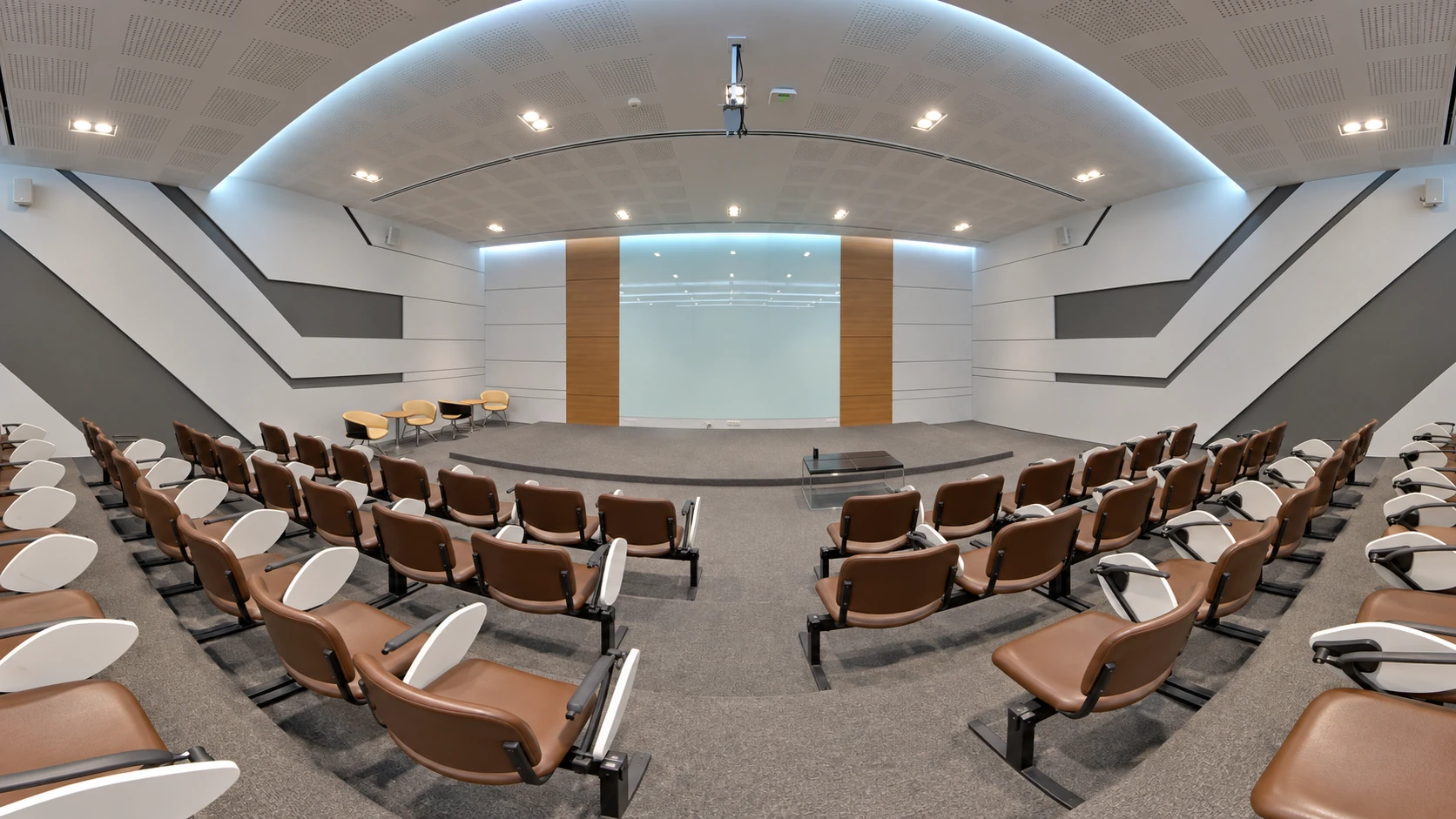 Auditorium with brown seats, white writing tablets and geometric acoustic panels